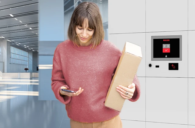 A person holding a cardboard box stands next to smart lockers in a bright, modern hall with large windows.